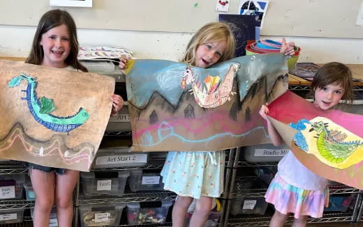 a couple of girls holding up a large piece of art