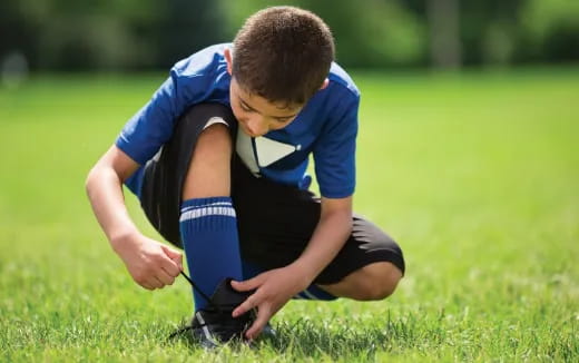 a boy kneeling in grass with a camera