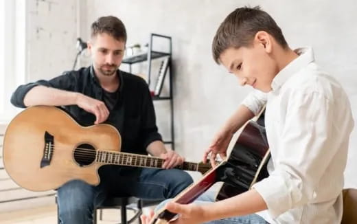 a person playing a guitar next to another man