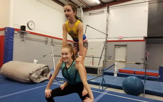 a woman standing on a man's back in a gym