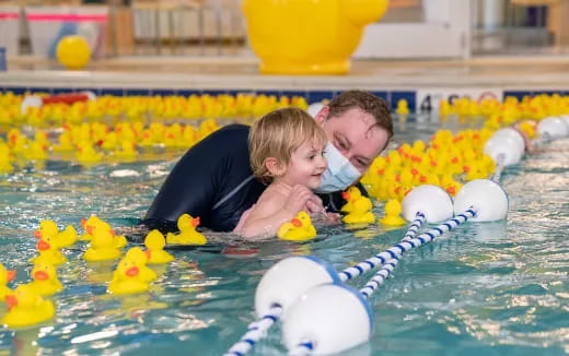 a person and a child in a pool with rubber ducks