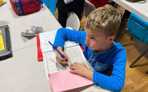 a boy sitting at a table writing on a piece of paper