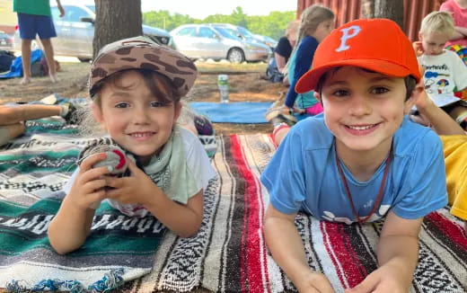 a couple of kids sitting on a blanket in a park