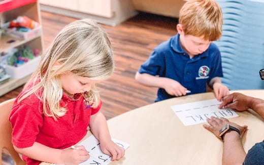 a boy and girl sitting at a table writing on paper