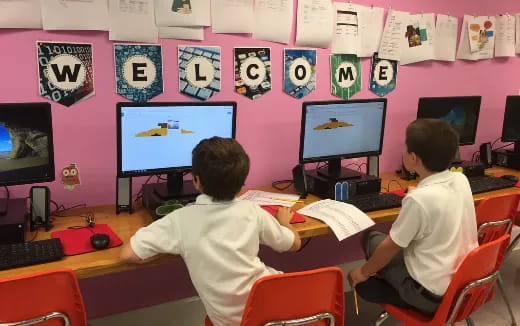 a couple of boys sitting at a desk with computers